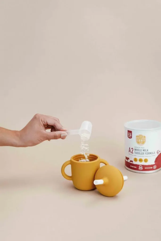 A hand pouring a scoop of formula into children's cup