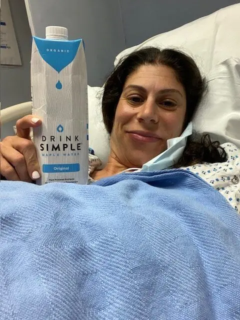 melissa in hospital bed, holding carton of drink simple maple water