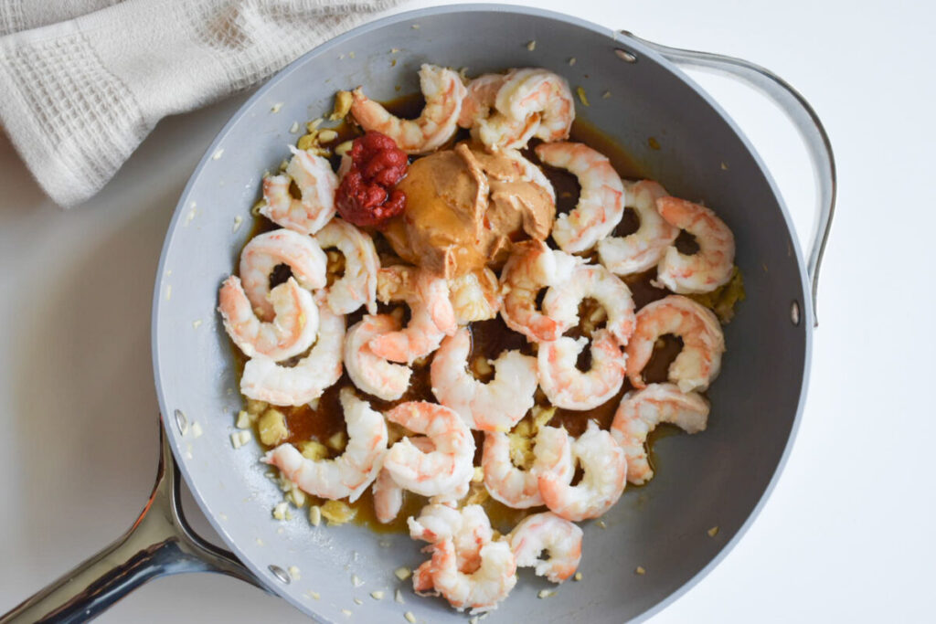 adding peanut butter and other sauce ingredients to pot with shrimp and aromatics