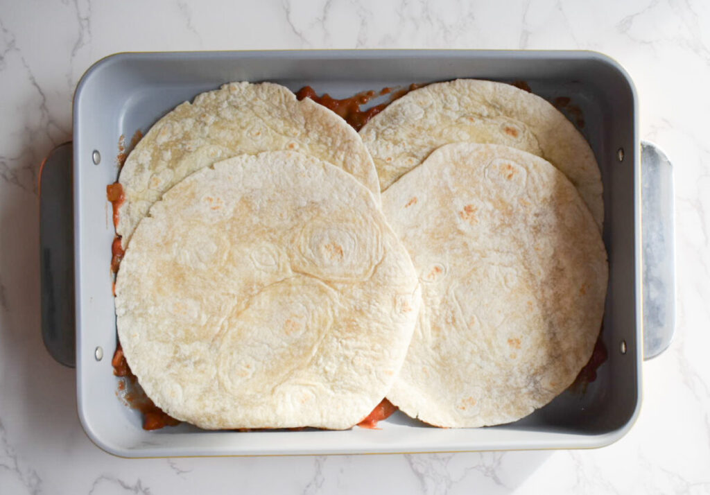 layers of tortilla and taco meat in taco bake dish