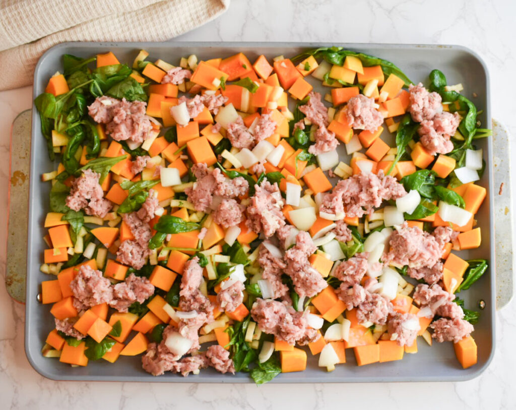 raw turkey, butternut squash, apples, and spinach on a sheet pan ready to be baked